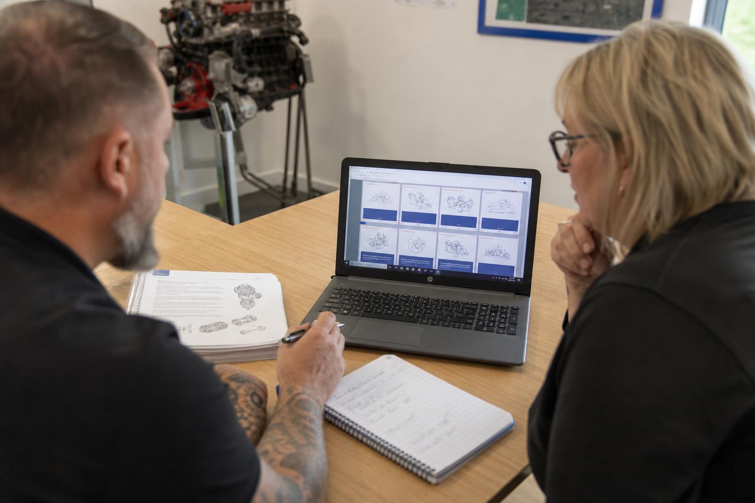 Learning designer and technical trainer reviewing a course storyboard on a laptop in a workshop office